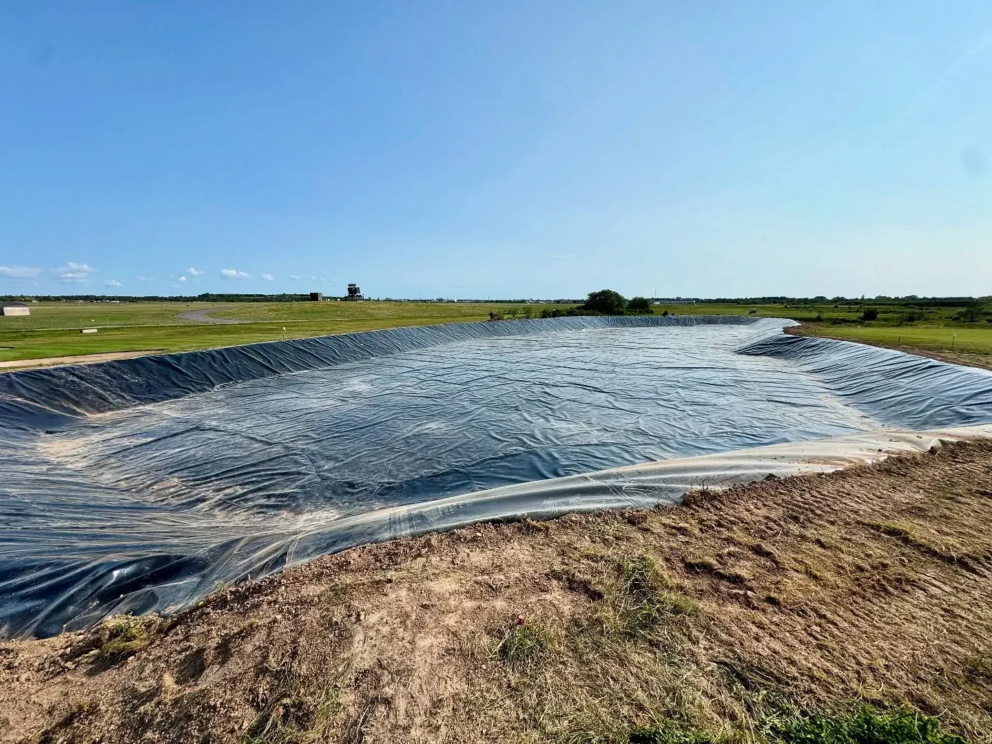 Bevattningsdamm under anläggning med utlagd geomembran i ett öppet fält